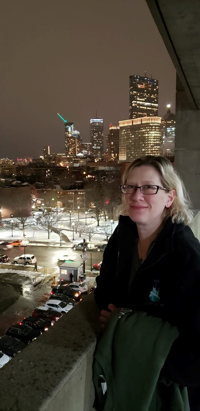 Abby Kingsbury in Boston with the nighttime city skyline behind her