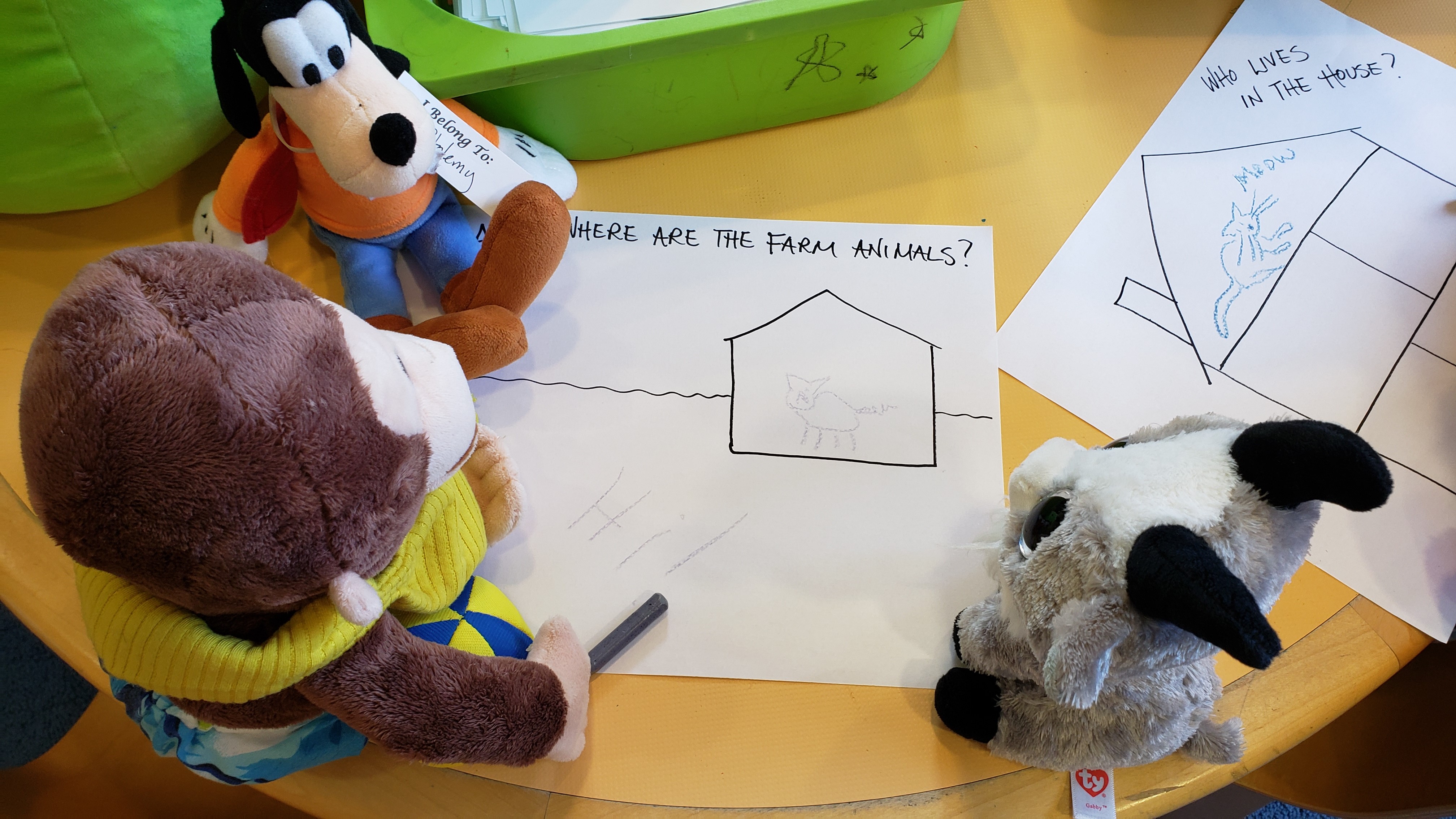 three stuffed animals sitting on a yellow table and coloring a piece of paper with crayons